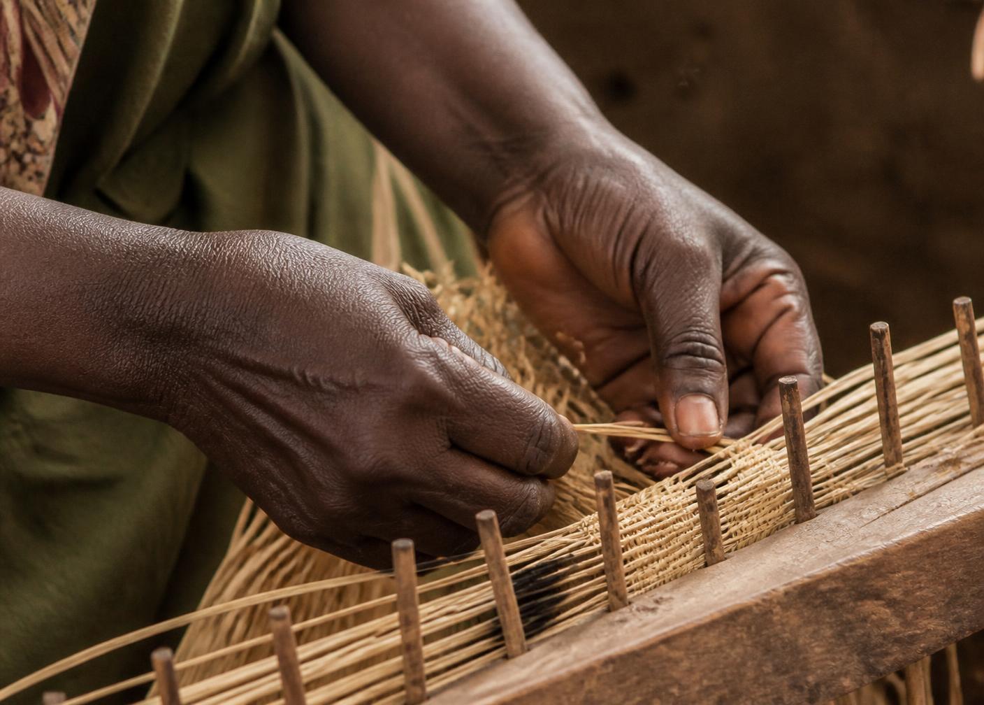 Hands weaving fine raffia fibre on a wooden loom